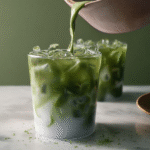 Glass of iced matcha latte with almond milk and ice cubes on wooden table